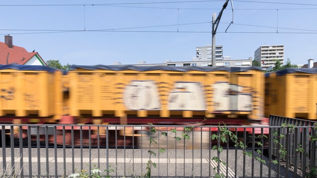 Ein Güterwagen fährt durch ein Wohngebiet. Vorne ist ein metallenes Gitter zu sehen. Der Güterwagen ist gelb. Ein Güterwagen fährt durch ein Wohngebiet. Vorne ist ein metallenes Gitter zu sehen. Der Güterwagen ist gelb.
