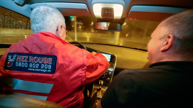 Fahrer mit Nez-Rouge-Weste und Fahrgast in Auto. Fahrer mit Nez-Rouge-Weste und Fahrgast in Auto.