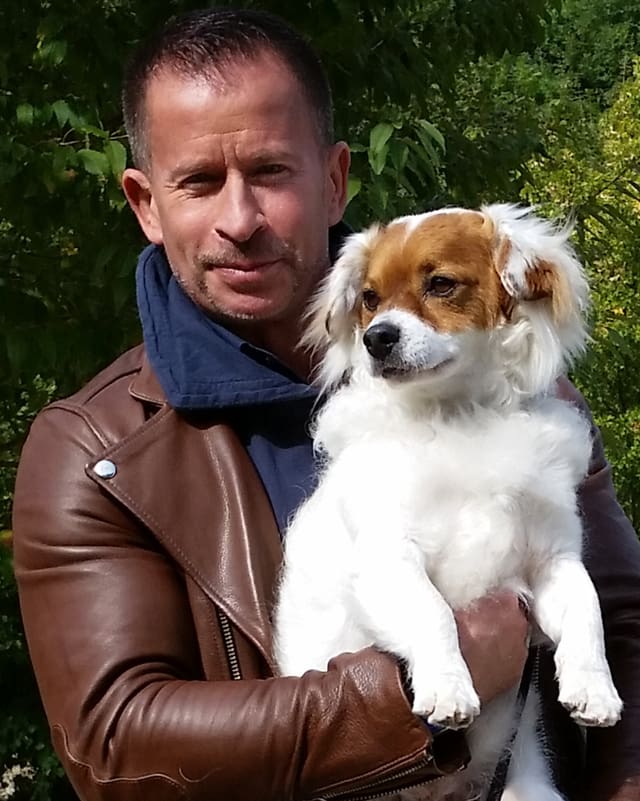 Leonard mit brauner Lederjacke und blauem Sweat-Shirt hält den weiss-braunen Hund auf dem Arm. Leonard mit brauner Lederjacke und blauem Sweat-Shirt hält den weiss-braunen Hund auf dem Arm.