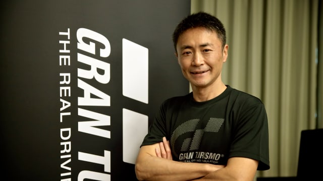 Yamauchi posiert vor dem Logo seines Spiels. Yamauchi posiert vor dem Logo seines Spiels.