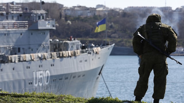 Ein Soldat steht beim Hafen mit Blick auf ein Kriegsschiff. Ein Soldat steht beim Hafen mit Blick auf ein Kriegsschiff.