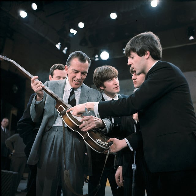 Der TV-Entertainer Es Sullivan hält eine Gitarre, Paul McCartney von den Beatles steht neben ihm. Der TV-Entertainer Es Sullivan hält eine Gitarre, Paul McCartney von den Beatles steht neben ihm.