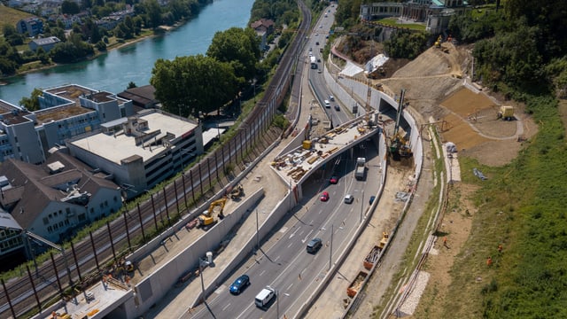 Man blickt von oben auf eine Strasse, auf der Autos fahren. Und ein Tunnel verschwindet rechts in einem Hügel. Man blickt von oben auf eine Strasse, auf der Autos fahren. Und ein Tunnel verschwindet rechts in einem Hügel.