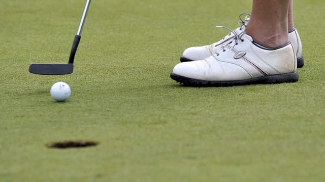 Ein Golfball steht wenige Zentimeter vor einem Golfloch. Ein Golfball steht wenige Zentimeter vor einem Golfloch.