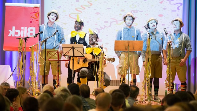 Eine verkleidete Gruppe junger Männer singt auf der Bühne. Eine verkleidete Gruppe junger Männer singt auf der Bühne.