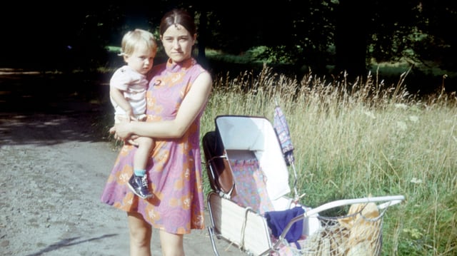 AUf einer alten Aufnahme hält eine junge Mutter ein Kind im Arm. AUf einer alten Aufnahme hält eine junge Mutter ein Kind im Arm.
