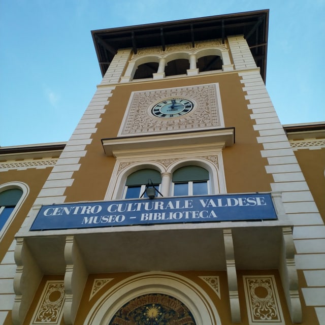 Ein Turm mit Ziffernblatt und der Aufschrift "Centro Culturale Valdese. Museo – Biblioteca" Ein Turm mit Ziffernblatt und der Aufschrift "Centro Culturale Valdese. Museo – Biblioteca"