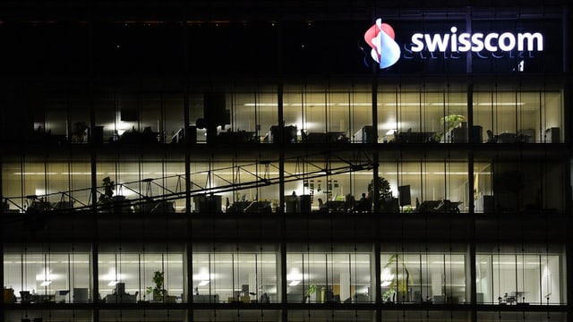 Mehrstöckiges, transparentes Gebäude mit Swisscom-Logo: Es ist dunkel und in den Büros wird gearbeitet. Mehrstöckiges, transparentes Gebäude mit Swisscom-Logo: Es ist dunkel und in den Büros wird gearbeitet.