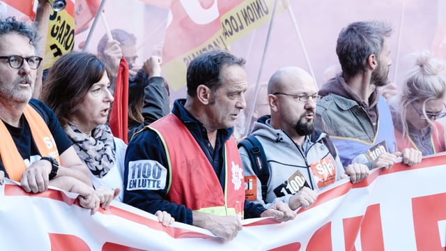 Ein Arbeiterprotest: Leute halten ein langes Plakat und demonstrieren in greller Kleidung. Ein Arbeiterprotest: Leute halten ein langes Plakat und demonstrieren in greller Kleidung.
