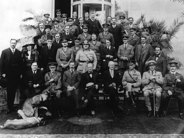 Gruppenbild mit mehrheitlich Männern in teils militärischen Anzügen. Gruppenbild mit mehrheitlich Männern in teils militärischen Anzügen.