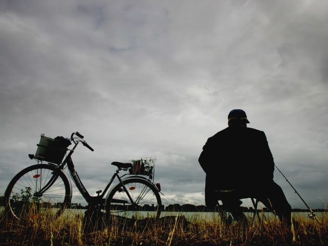 Man sitzt am Ufer eines Flusses und hofft auf einen Fang. Der Himmel ist wolkenverhangen. Man sitzt am Ufer eines Flusses und hofft auf einen Fang. Der Himmel ist wolkenverhangen.