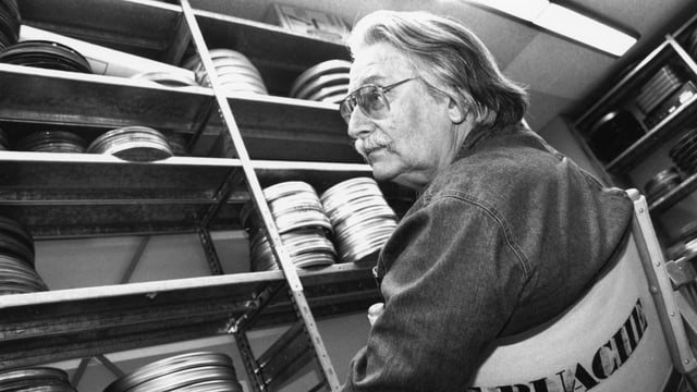 Ein Mann sitzt im Archiv, auf den Gestellen liegen viele Filmkassetten. Ein Mann sitzt im Archiv, auf den Gestellen liegen viele Filmkassetten.