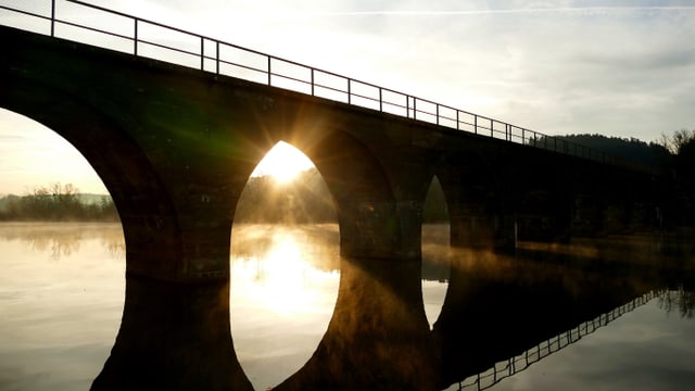 Die Sonne geht hinter der Brück über den Wohlensee auf.