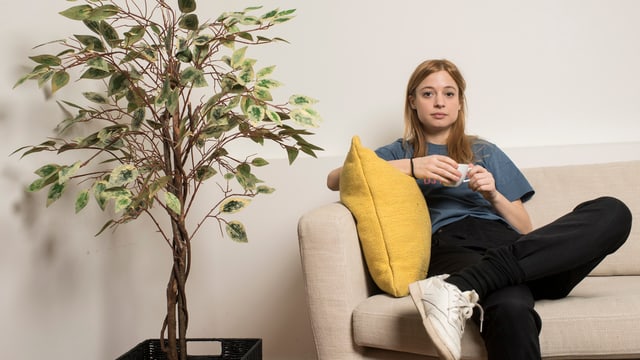 EIne Frau sitzt mt einer TAsse auf einem Sofa EIne Frau sitzt mt einer TAsse auf einem Sofa