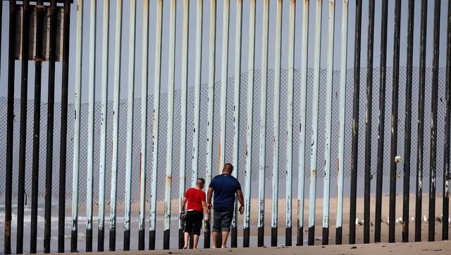 Zwei Personen vor dem Grenzzaun zwischen Mexiko und den USA Zwei Personen vor dem Grenzzaun zwischen Mexiko und den USA