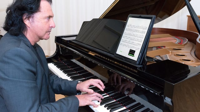 Ein Pianist spielt Klavier und schaut auf ein digitales Notenpult. Ein Pianist spielt Klavier und schaut auf ein digitales Notenpult.