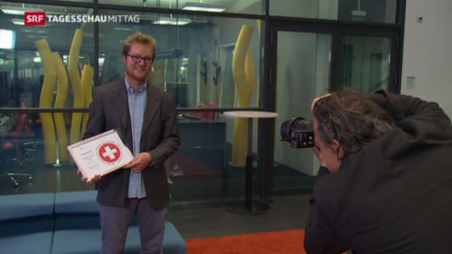 Eine Person wird vor einer Glaswand mit einer Urkunde fotografiert. Eine Person wird vor einer Glaswand mit einer Urkunde fotografiert.