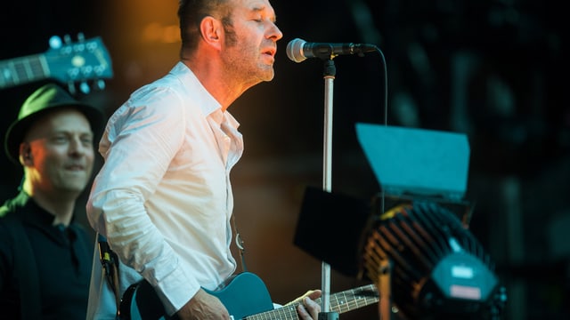Ein Mann mit Gitarre steht am Mikrofon und singt. Ein Mann mit Gitarre steht am Mikrofon und singt.
