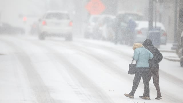 Zwei Menschen überqueren eine verschneite Strasse. Zwei Menschen überqueren eine verschneite Strasse.