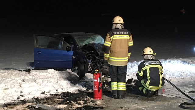 Zwei Feuerwehrmänner stehen, bzw. knien vor dem ausgebrannten Auto Zwei Feuerwehrmänner stehen, bzw. knien vor dem ausgebrannten Auto
