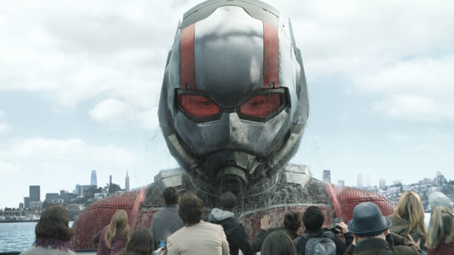 Ein riesiger Ant-Man kommt aus dem Wasser. Viele normal grosse Menschen schauen zu ihm hoch. Ein riesiger Ant-Man kommt aus dem Wasser. Viele normal grosse Menschen schauen zu ihm hoch.