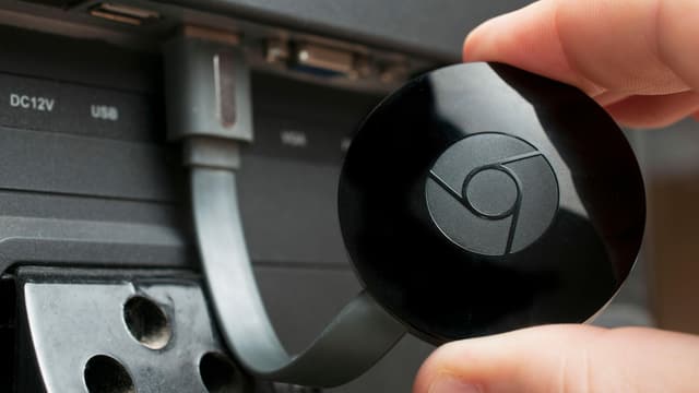 Eine Hand hält eine kleine runde schwarze Scheibe, die an einem TV angeschlossen ist. Eine Hand hält eine kleine runde schwarze Scheibe, die an einem TV angeschlossen ist.
