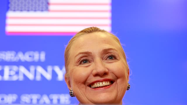 Clinton lächelnd vor blauer Wand mit US-Flagge. Clinton lächelnd vor blauer Wand mit US-Flagge.