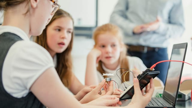 Mädchen an einem Tisch mit einem Handy und Kabeln in der Hand. Mädchen an einem Tisch mit einem Handy und Kabeln in der Hand.
