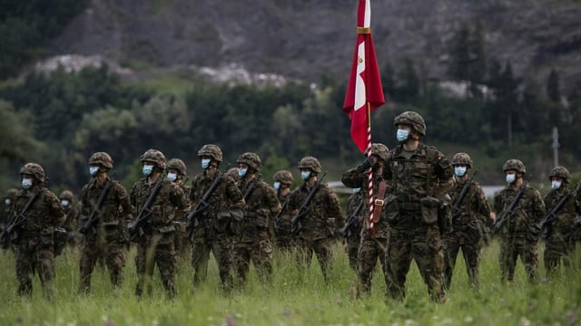 Soldaten (mit Gesichtsmaske) stehen in einem Feld, einer hält eine Schweizer Fahne. Soldaten (mit Gesichtsmaske) stehen in einem Feld, einer hält eine Schweizer Fahne.