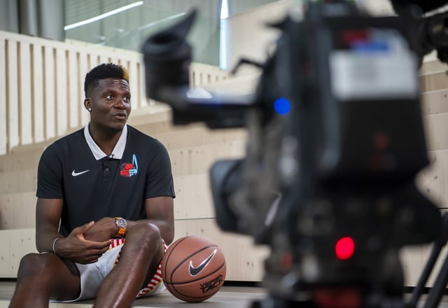 Clint Capela sitzt neben einem Basketball, eine Filmkamera nimmt ihn dabei auf Clint Capela sitzt neben einem Basketball, eine Filmkamera nimmt ihn dabei auf