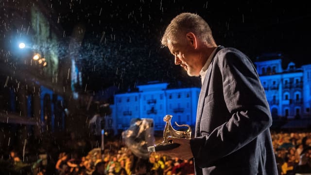 Ein Mann mit einer goldenen Leopardenstatue geht im Regen eine Treppe hinunter. Ein Mann mit einer goldenen Leopardenstatue geht im Regen eine Treppe hinunter.