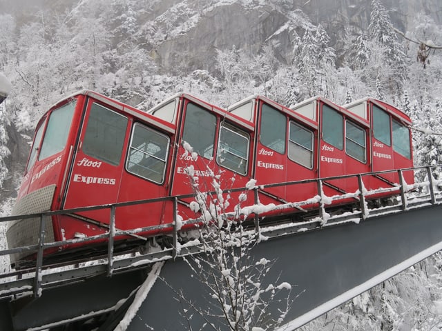 Eine alte rote Zahnradbahn vor Winterkulisse in steilem Gelände. 