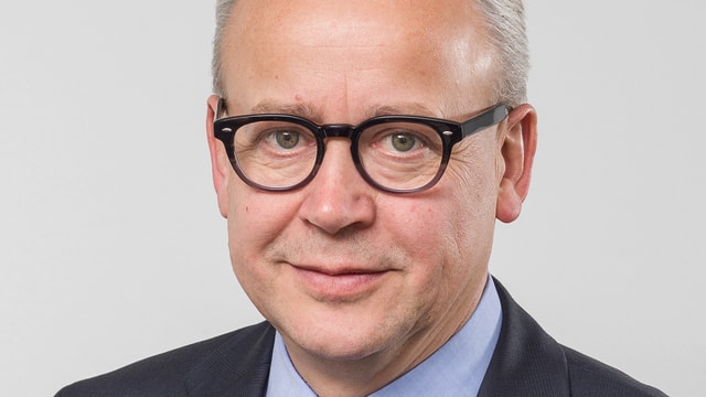 Ein Mann mit grauen Haaren und schwarzer Brille lächelt in die Kamera. Ein Mann mit grauen Haaren und schwarzer Brille lächelt in die Kamera.