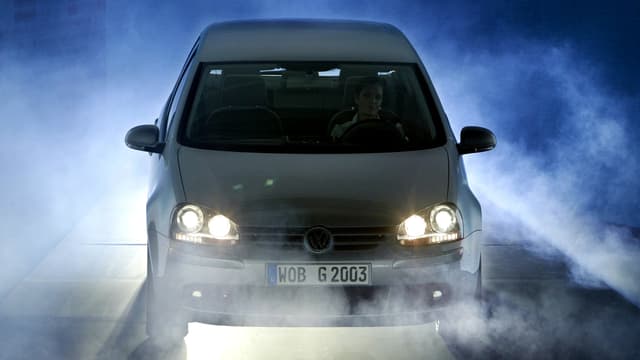 Ein weisser Golf steht mit brennenden Lichtern in dichtem Nebel. Ein weisser Golf steht mit brennenden Lichtern in dichtem Nebel.