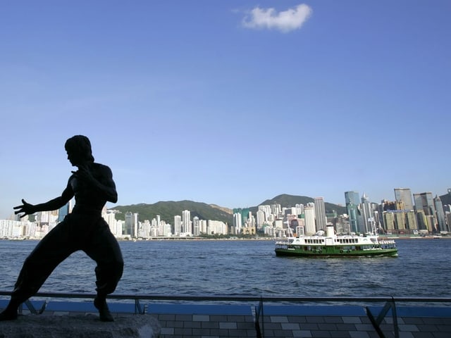 eine Statue von einem kämpfenden Mann vor einer Bucht, im Hintergrund die Skyline von Hong Kong.