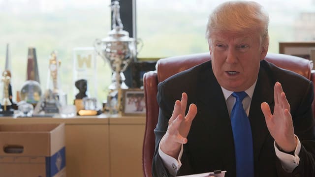 Trump an einem Schreibtisch sitzend und mit den Händen gestikulierend. Trump an einem Schreibtisch sitzend und mit den Händen gestikulierend.