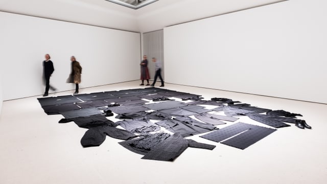 Ein Museumsraum: Auf dem Boden sind schwarze Kleider ausgebreitet. Ein Museumsraum: Auf dem Boden sind schwarze Kleider ausgebreitet.