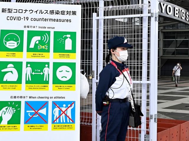 Frau vor Plakat mit Corona-Schutzmassnahmen in Tokio Frau vor Plakat mit Corona-Schutzmassnahmen in Tokio
