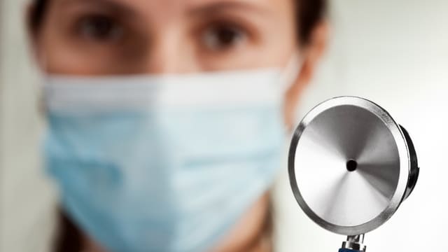 Ärztin mit Mundschutz hält ihr Stethoskop in die Kamera Ärztin mit Mundschutz hält ihr Stethoskop in die Kamera