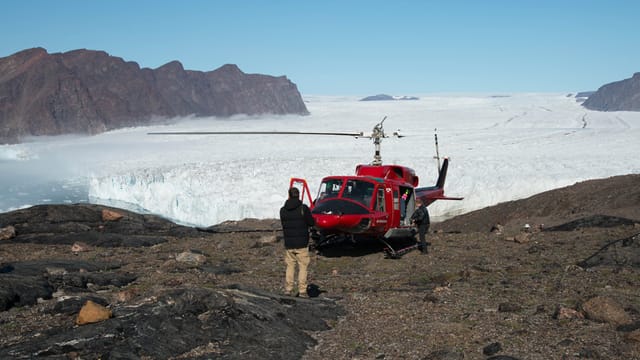 Ein roter Bell-Helikopter auf felsigem Grund. Im Hintergrund die Eisfläche des Bowdoin-Gletschers. Ein roter Bell-Helikopter auf felsigem Grund. Im Hintergrund die Eisfläche des Bowdoin-Gletschers.