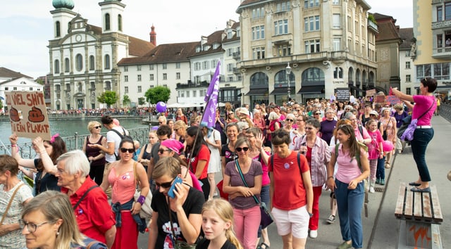 Frauen in farbigen Kleidern und Fahnen laufen über eine Brücke Frauen in farbigen Kleidern und Fahnen laufen über eine Brücke