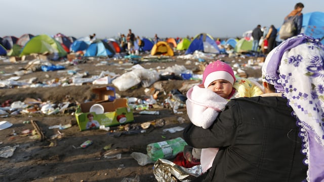 Mutter mit Baby schaut auf eine Zeltstadt Mutter mit Baby schaut auf eine Zeltstadt