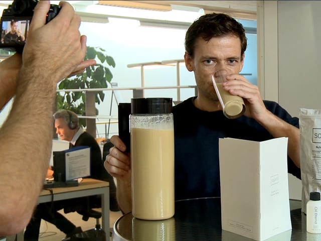 Ein Mann trinkt aus einem Glas, ein anderer Mann filmt ihn dabei mit einer Kamera. Ein Mann trinkt aus einem Glas, ein anderer Mann filmt ihn dabei mit einer Kamera.