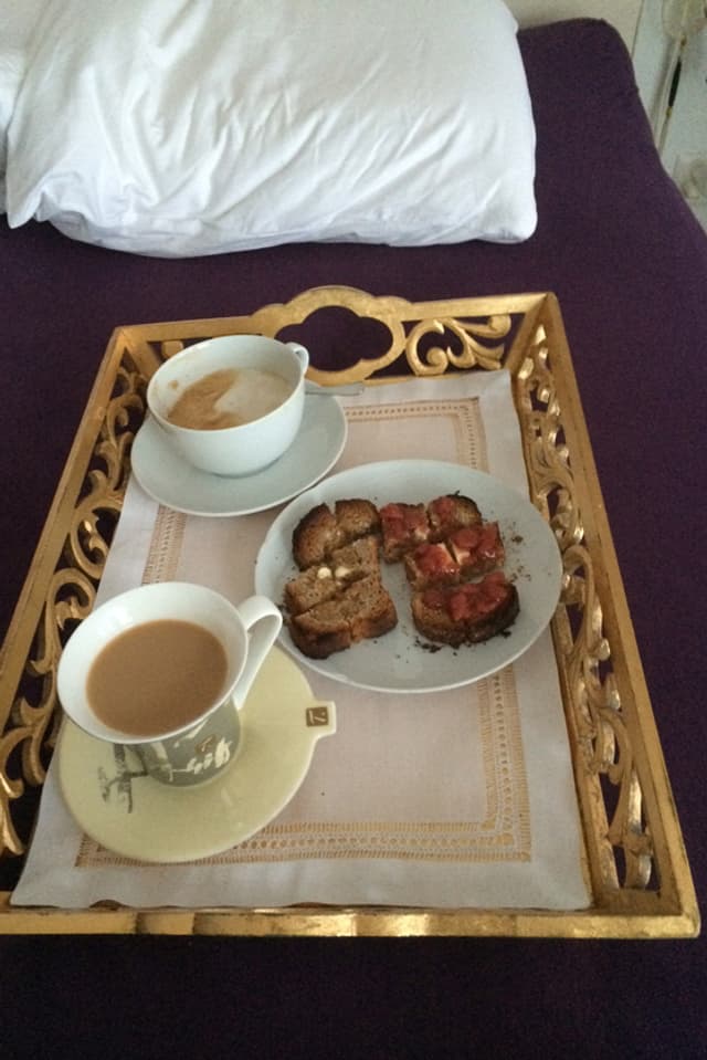 Tablett auf dem Bett mit Kaffe und Brötchen.