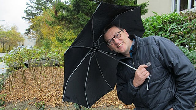 Mann mit Brille hält einen schwarzen Regenschirm und lacht in die Kamera. Mann mit Brille hält einen schwarzen Regenschirm und lacht in die Kamera.