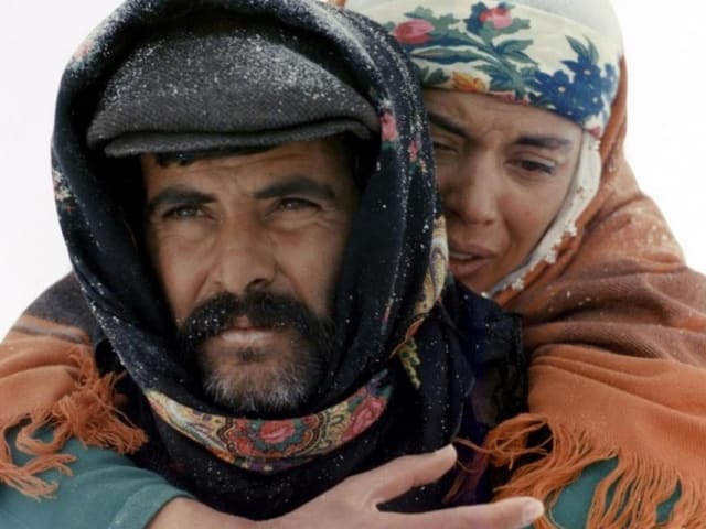 FIlmstill: Ein Mann trägt eine Frau auf dem Rücken. FIlmstill: Ein Mann trägt eine Frau auf dem Rücken.