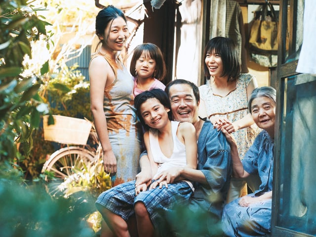 Eine sechsköpfige Familie sitzt lachend vor einem Haus Eine sechsköpfige Familie sitzt lachend vor einem Haus