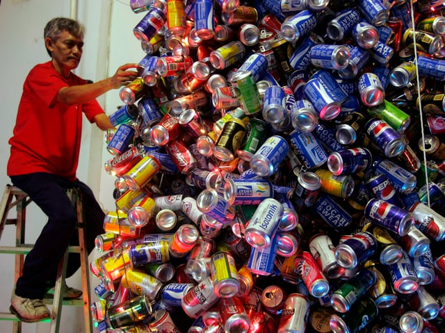 Mann befestigt Getränkedosen so, dass ein Weihnachtsbaum entsteht