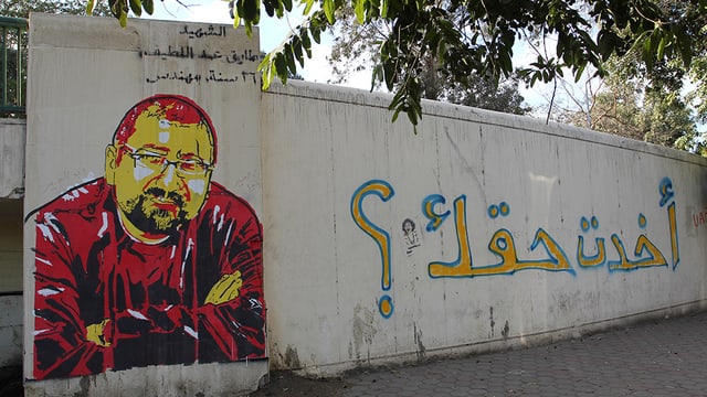 Abbildung eines Graffitos auf einer Mauer: Portrait eines Mannes mit Brille und Bart, der die Arme vor dem Körper verschrämkt hält. Abbildung eines Graffitos auf einer Mauer: Portrait eines Mannes mit Brille und Bart, der die Arme vor dem Körper verschrämkt hält.