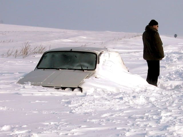 Die grossen Schneeverwehungen haben ein Auto komplett blockiert. Ein Mann steht vor dem Auto und starrt in die kalte Winterlandschaft. Die grossen Schneeverwehungen haben ein Auto komplett blockiert. Ein Mann steht vor dem Auto und starrt in die kalte Winterlandschaft.